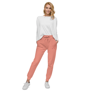 Female model wearing coral pink 'Girl Power' sweatpants with pink, orange, and red embroidered symbols by maillot.co - unisex sizing fleece joggers